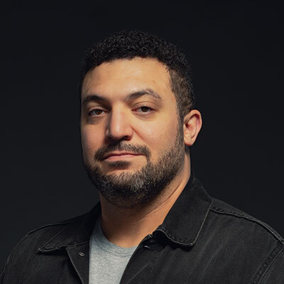Studio portrait of a Veteran wearing a gray shirt and dark jacket against a dark background