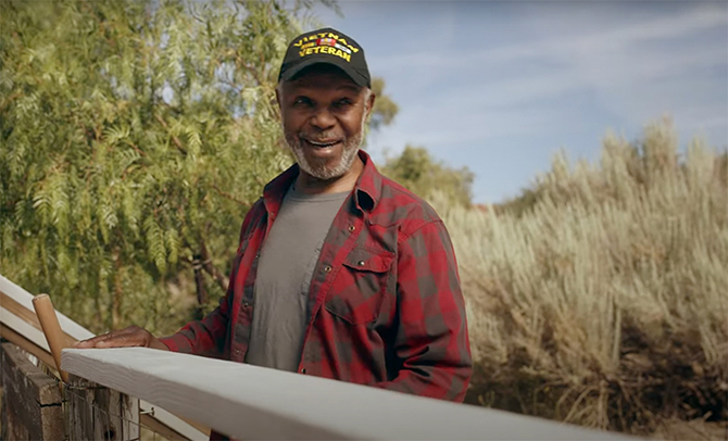 Veteran working on fence outdoors smiling to man off camera