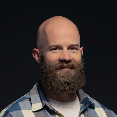 Studio portrait of a Veteran wearing a gray shirt and dark jacket against a dark background